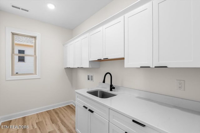 clothes washing area featuring cabinets, hookup for a washing machine, light hardwood / wood-style flooring, and sink