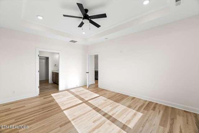 unfurnished bedroom featuring a tray ceiling, light hardwood / wood-style flooring, and ensuite bathroom