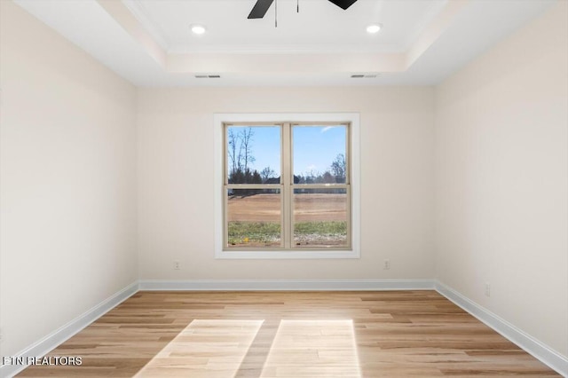 spare room with ceiling fan, light wood-type flooring, and a tray ceiling