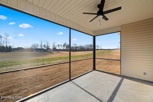 unfurnished sunroom with ceiling fan and a rural view