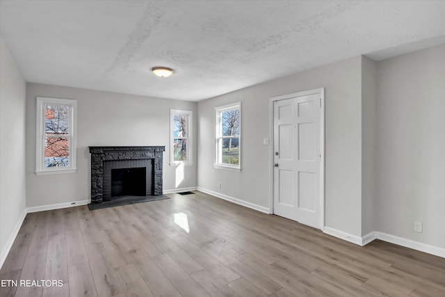 unfurnished living room with a textured ceiling, a brick fireplace, and light wood-type flooring