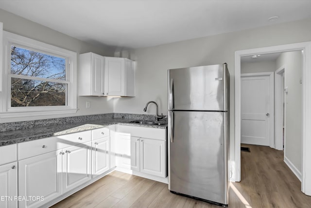 kitchen featuring white cabinets, stainless steel fridge, sink, and dark stone countertops