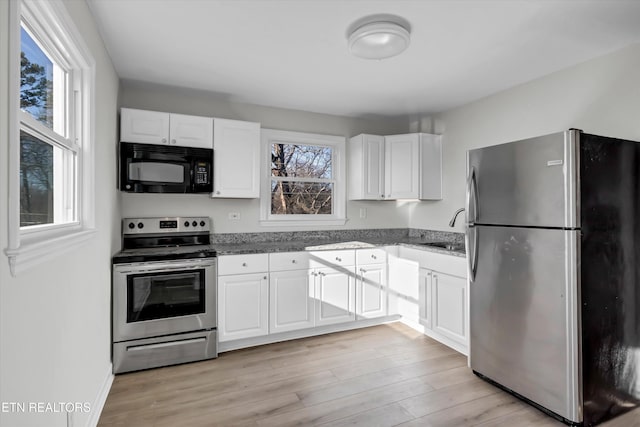 kitchen featuring white cabinets, stainless steel appliances, dark stone counters, sink, and light wood-type flooring