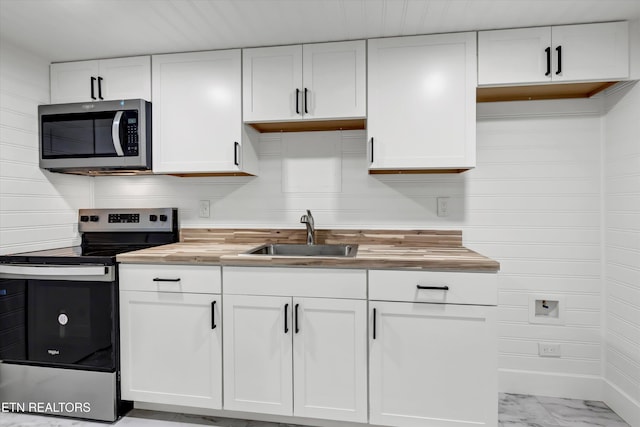 kitchen featuring appliances with stainless steel finishes, white cabinetry, wooden counters, and sink