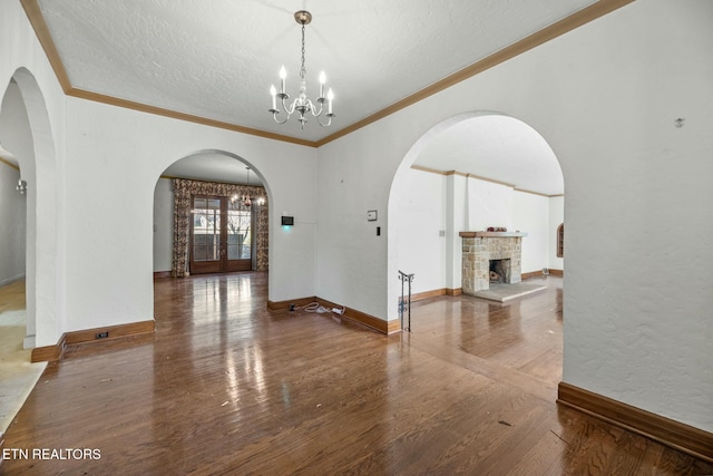 interior space with a stone fireplace, hardwood / wood-style floors, an inviting chandelier, ornamental molding, and a textured ceiling