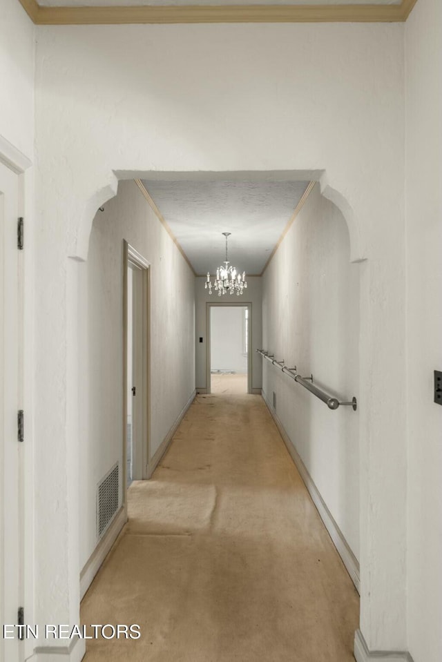 corridor with ornamental molding, light carpet, and a chandelier