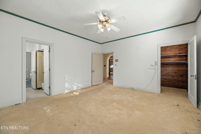 unfurnished bedroom with ceiling fan, a closet, a textured ceiling, and a walk in closet