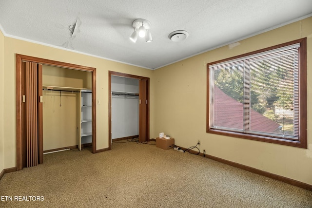 unfurnished bedroom with multiple closets, crown molding, carpet floors, and a textured ceiling