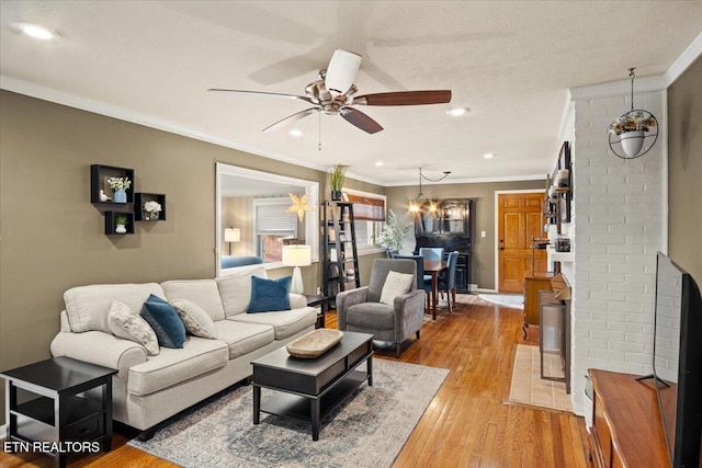 living room with light hardwood / wood-style floors, a textured ceiling, ornamental molding, and ceiling fan with notable chandelier