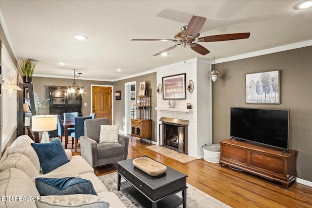 living room with a brick fireplace, ceiling fan with notable chandelier, ornamental molding, and light wood-type flooring