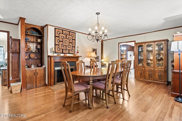 dining room featuring a textured ceiling, light hardwood / wood-style flooring, ornamental molding, and an inviting chandelier