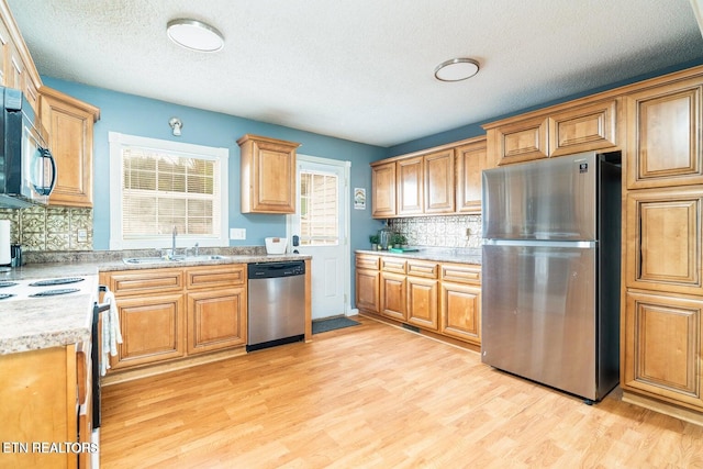 kitchen featuring appliances with stainless steel finishes, light hardwood / wood-style floors, tasteful backsplash, and sink