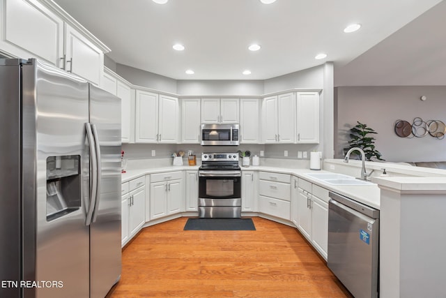 kitchen with kitchen peninsula, light wood-type flooring, stainless steel appliances, sink, and white cabinetry