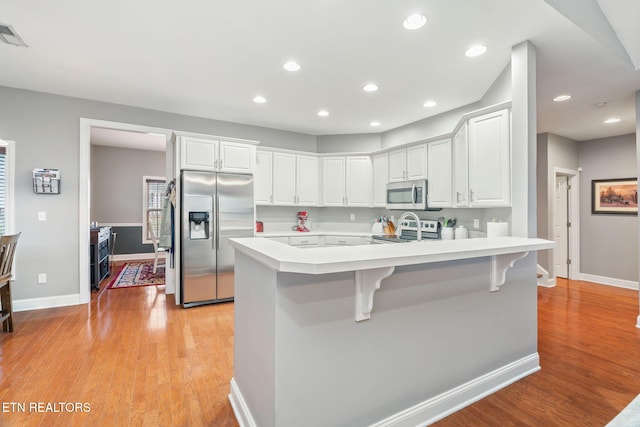 kitchen with white cabinetry, stainless steel appliances, a kitchen breakfast bar, kitchen peninsula, and light hardwood / wood-style floors