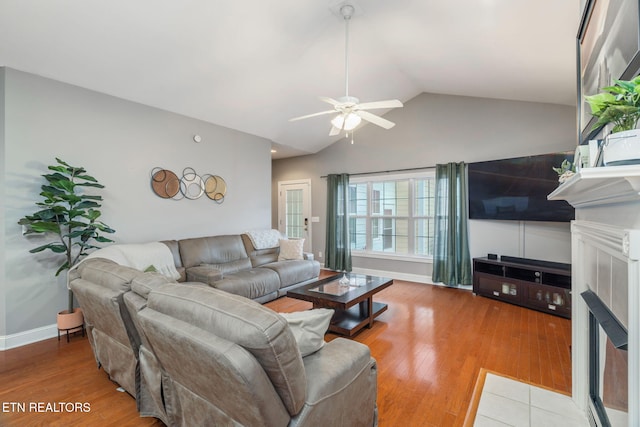 living room featuring a tile fireplace, hardwood / wood-style flooring, vaulted ceiling, and ceiling fan