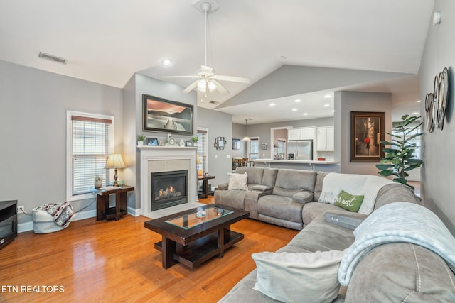 living room featuring ceiling fan, light wood-type flooring, lofted ceiling, and a tiled fireplace