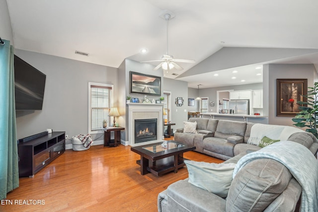 living room with light hardwood / wood-style floors, vaulted ceiling, and ceiling fan