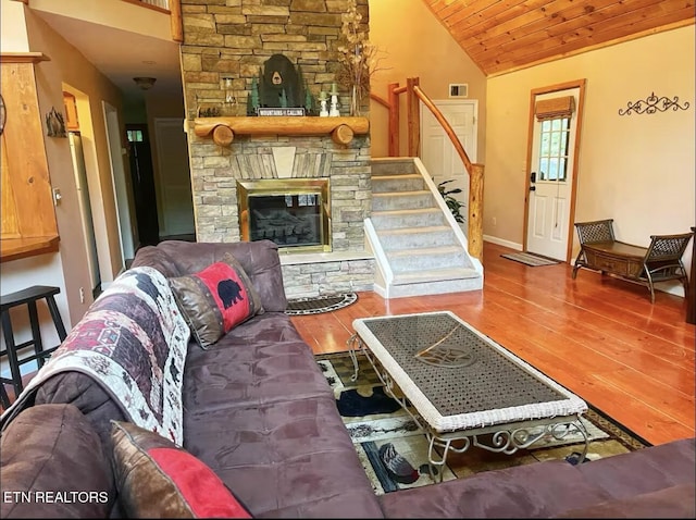 living room featuring hardwood / wood-style flooring, a stone fireplace, lofted ceiling, and wood ceiling