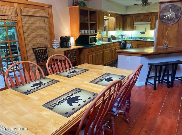 kitchen with a kitchen bar, gas stovetop, ceiling fan, and dark wood-type flooring