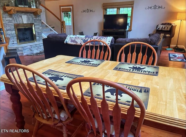 dining room with a stone fireplace and hardwood / wood-style flooring