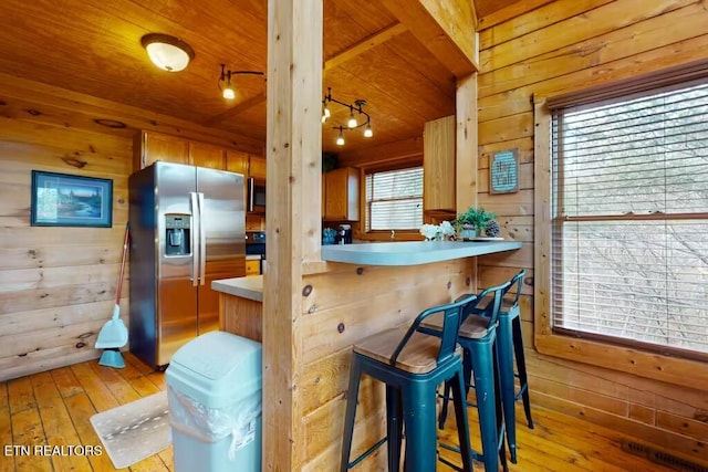 kitchen featuring appliances with stainless steel finishes, light hardwood / wood-style flooring, a breakfast bar area, and wood walls