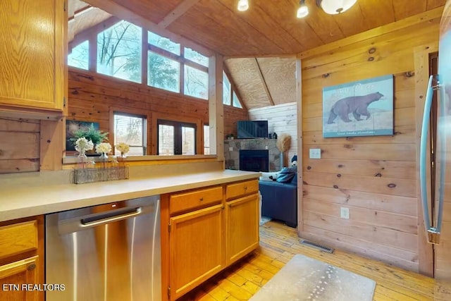 kitchen featuring wooden ceiling, wood walls, vaulted ceiling, a fireplace, and appliances with stainless steel finishes