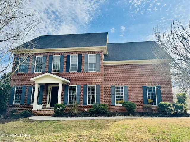 view of front of property with brick siding, roof with shingles, and a front yard