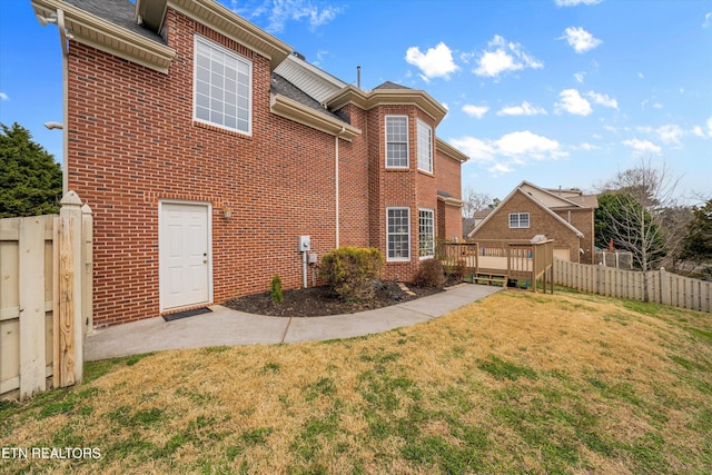 rear view of house with brick siding, a deck, a lawn, and fence