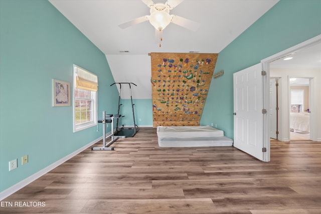 workout area featuring wood finished floors, visible vents, baseboards, ceiling fan, and vaulted ceiling