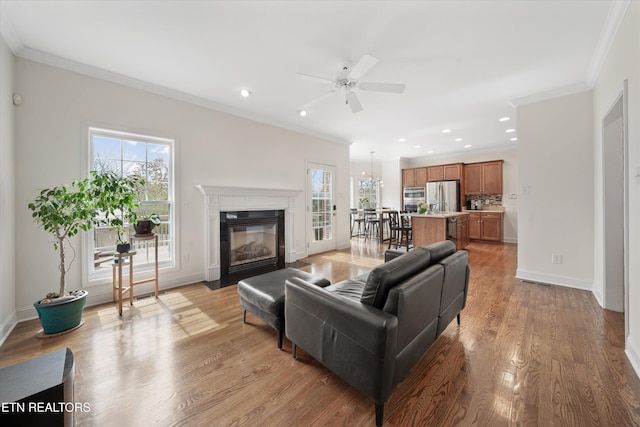 living room with light wood-style flooring, ornamental molding, and a ceiling fan