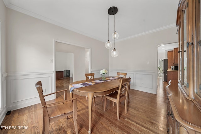 dining space featuring a wainscoted wall, ornamental molding, and wood finished floors