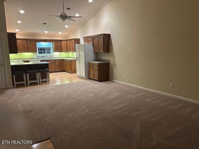 kitchen featuring a breakfast bar, lofted ceiling, white refrigerator with ice dispenser, ceiling fan, and ornamental molding