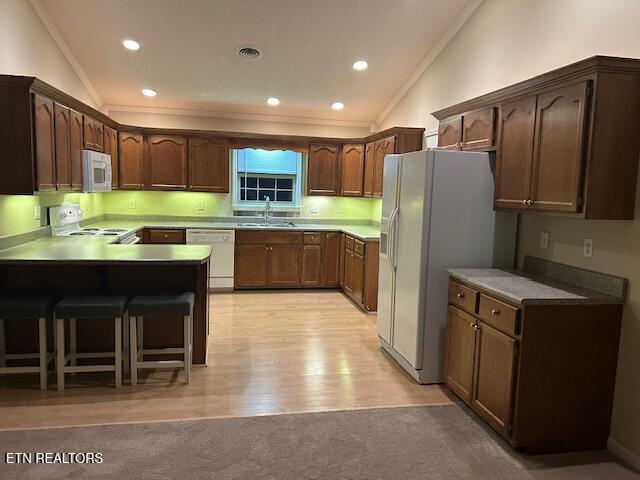 kitchen featuring sink, light hardwood / wood-style flooring, kitchen peninsula, lofted ceiling, and white appliances