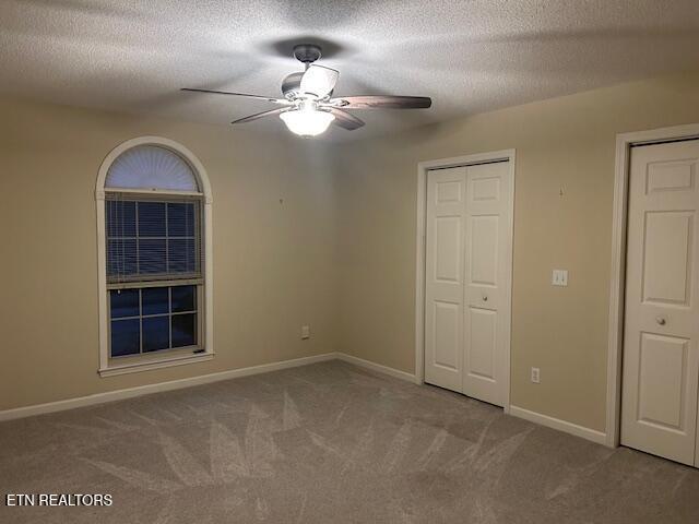 unfurnished bedroom with a textured ceiling, ceiling fan, light carpet, and two closets