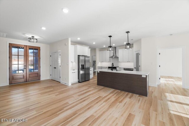 kitchen featuring white cabinetry, light hardwood / wood-style flooring, stainless steel fridge, pendant lighting, and a kitchen island with sink