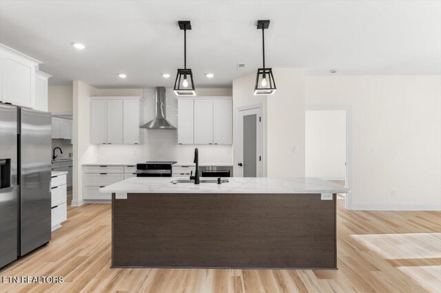 kitchen featuring white cabinetry, wall chimney range hood, an island with sink, and appliances with stainless steel finishes