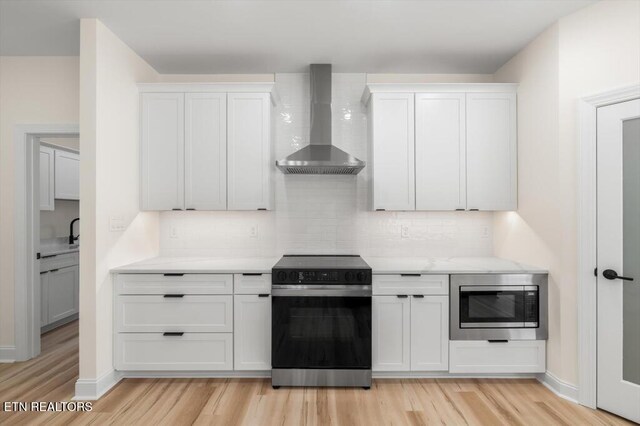 kitchen with white cabinets, appliances with stainless steel finishes, light wood-type flooring, and wall chimney range hood