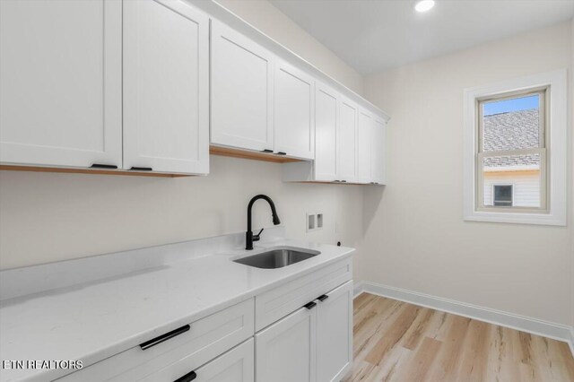 clothes washing area featuring cabinets, sink, washer hookup, and light hardwood / wood-style floors