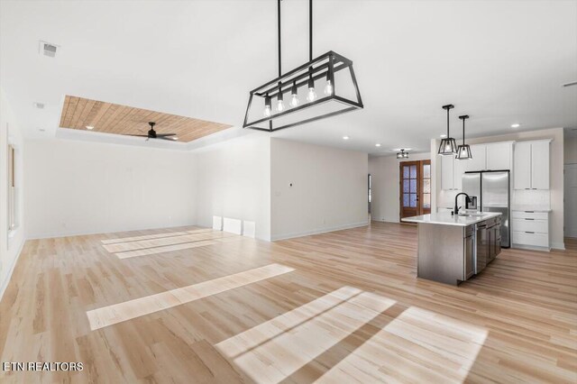 kitchen with white cabinetry, ceiling fan, light hardwood / wood-style flooring, pendant lighting, and a center island with sink