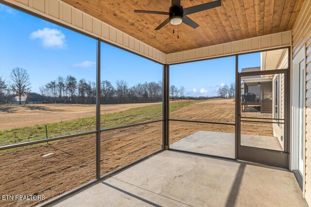 unfurnished sunroom featuring ceiling fan, wooden ceiling, and a rural view