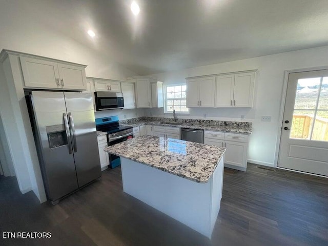 kitchen with light stone countertops, appliances with stainless steel finishes, a center island, dark hardwood / wood-style floors, and white cabinetry