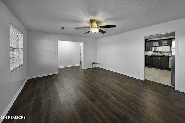 empty room with a textured ceiling, ceiling fan, dark hardwood / wood-style flooring, and sink