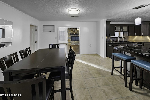 tiled dining space with sink, a textured ceiling, and a stone fireplace