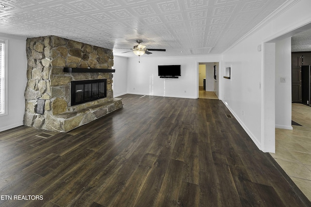 unfurnished living room featuring dark wood-type flooring, ceiling fan, and a stone fireplace