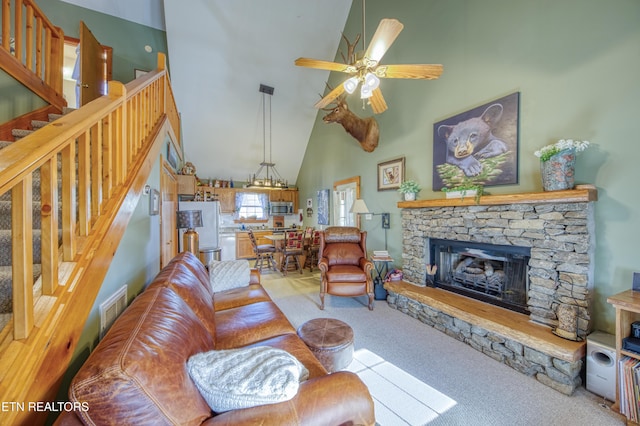 living room with carpet, ceiling fan, a stone fireplace, and high vaulted ceiling