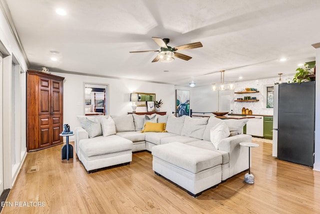 living room featuring light hardwood / wood-style floors, ornamental molding, and ceiling fan