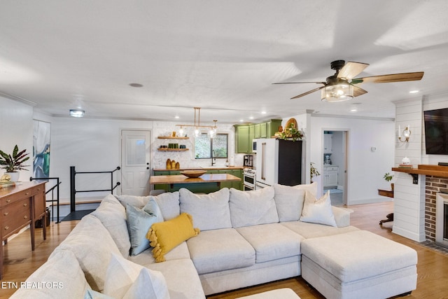 living room featuring ceiling fan, wood-type flooring, ornamental molding, and a fireplace