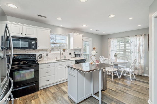 kitchen with black appliances, light hardwood / wood-style floors, white cabinetry, and sink