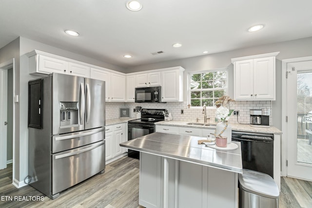 kitchen featuring a healthy amount of sunlight, sink, stainless steel counters, black appliances, and white cabinets