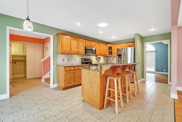 kitchen with decorative light fixtures, a center island with sink, a kitchen breakfast bar, stainless steel appliances, and light stone countertops